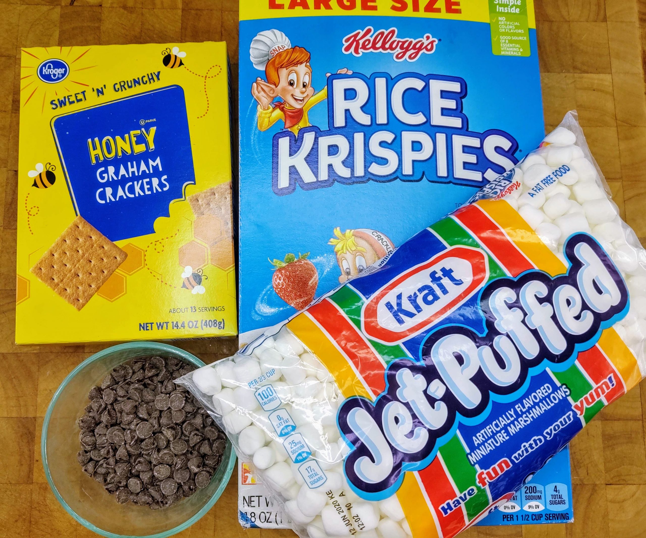 a box of rice krispie treats, a box of graham crackers, bag of jet puffed marshmallows, bowl of chocolate chips