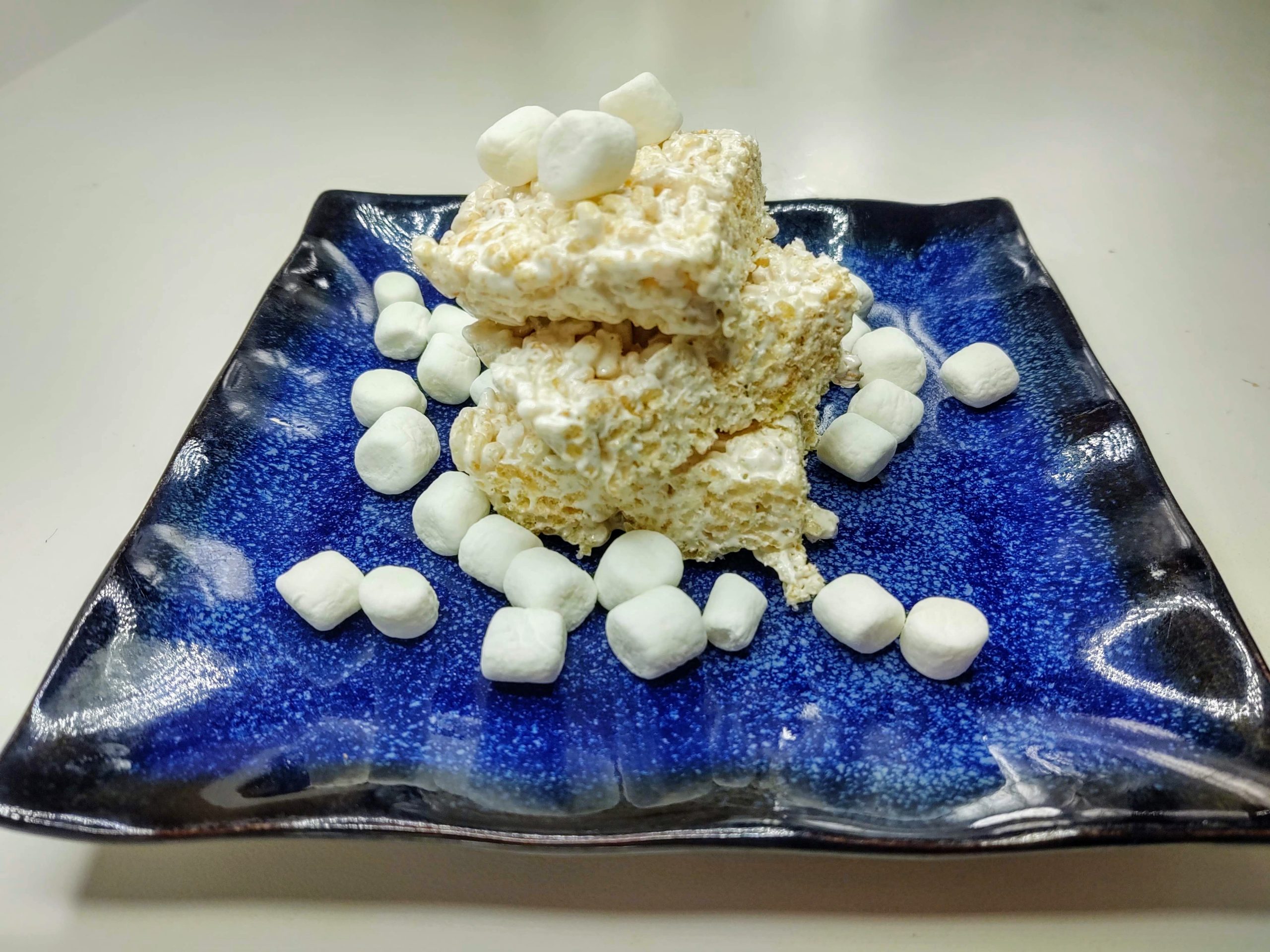 blue plate of frozen rice krispie treats with mini marshmallows sprinkled around
