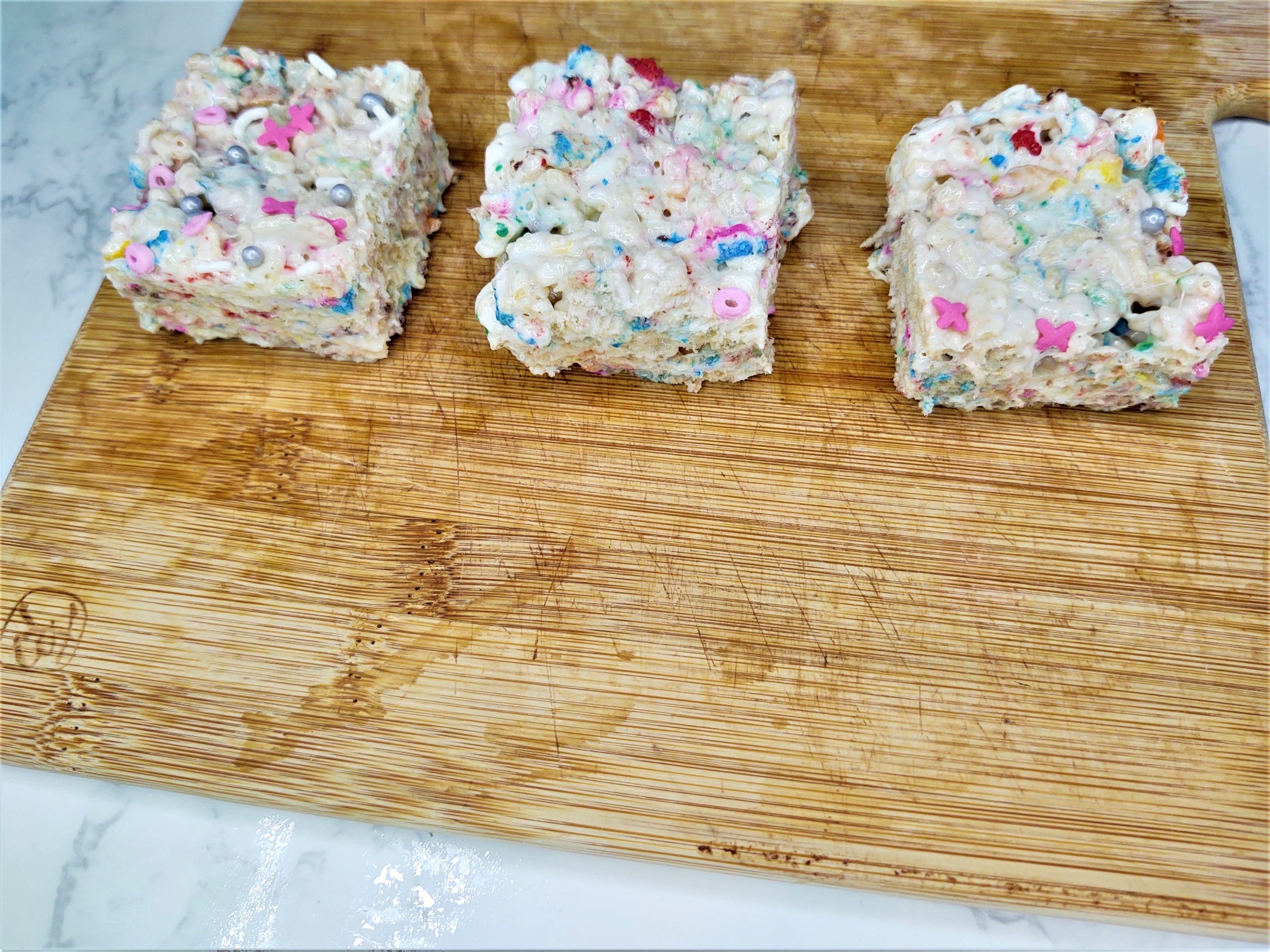 three rice krispie treats with sprinkles on a cutting board