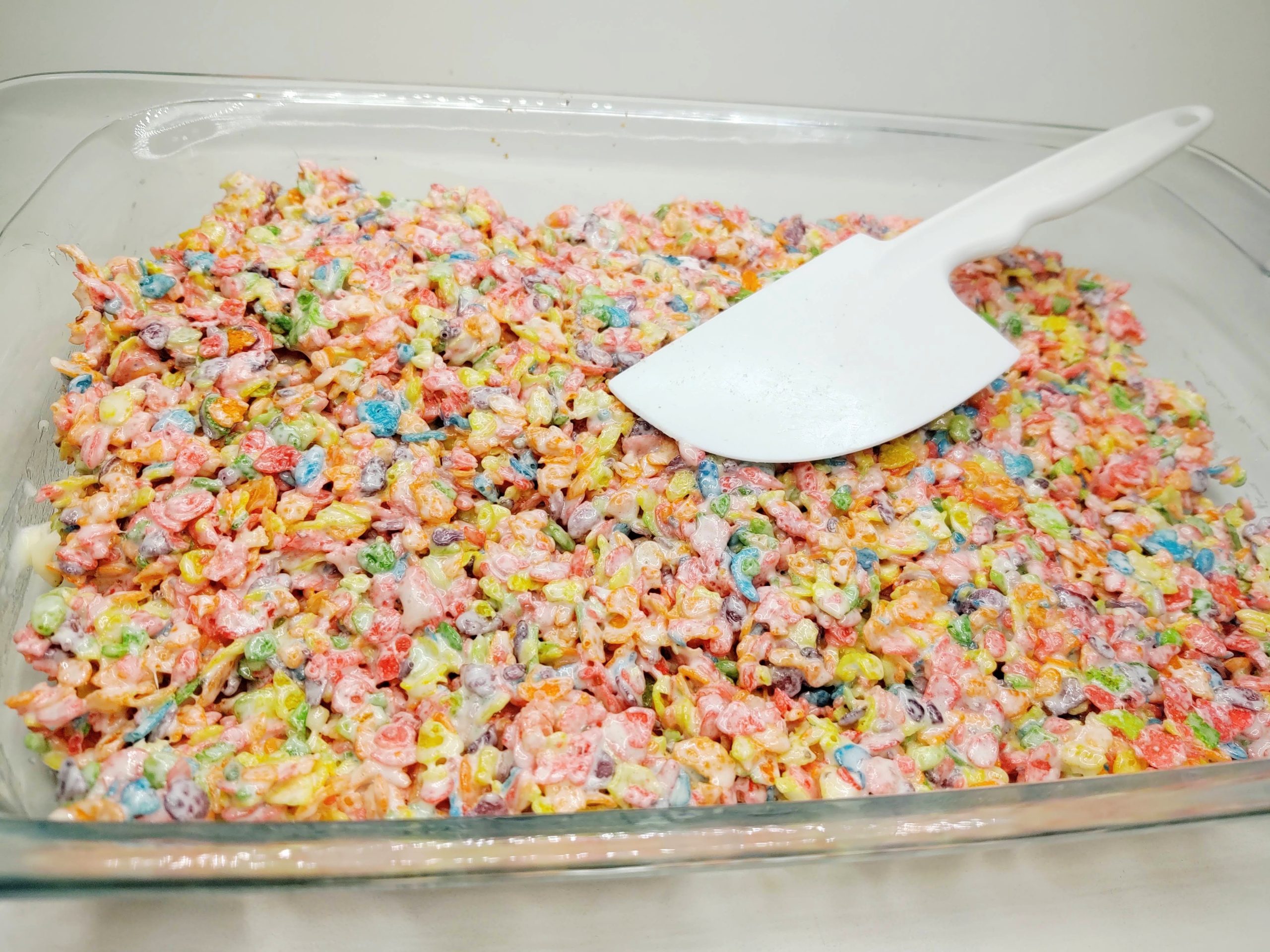 fruity pebble rice krispie treats in a pan with spatula on top