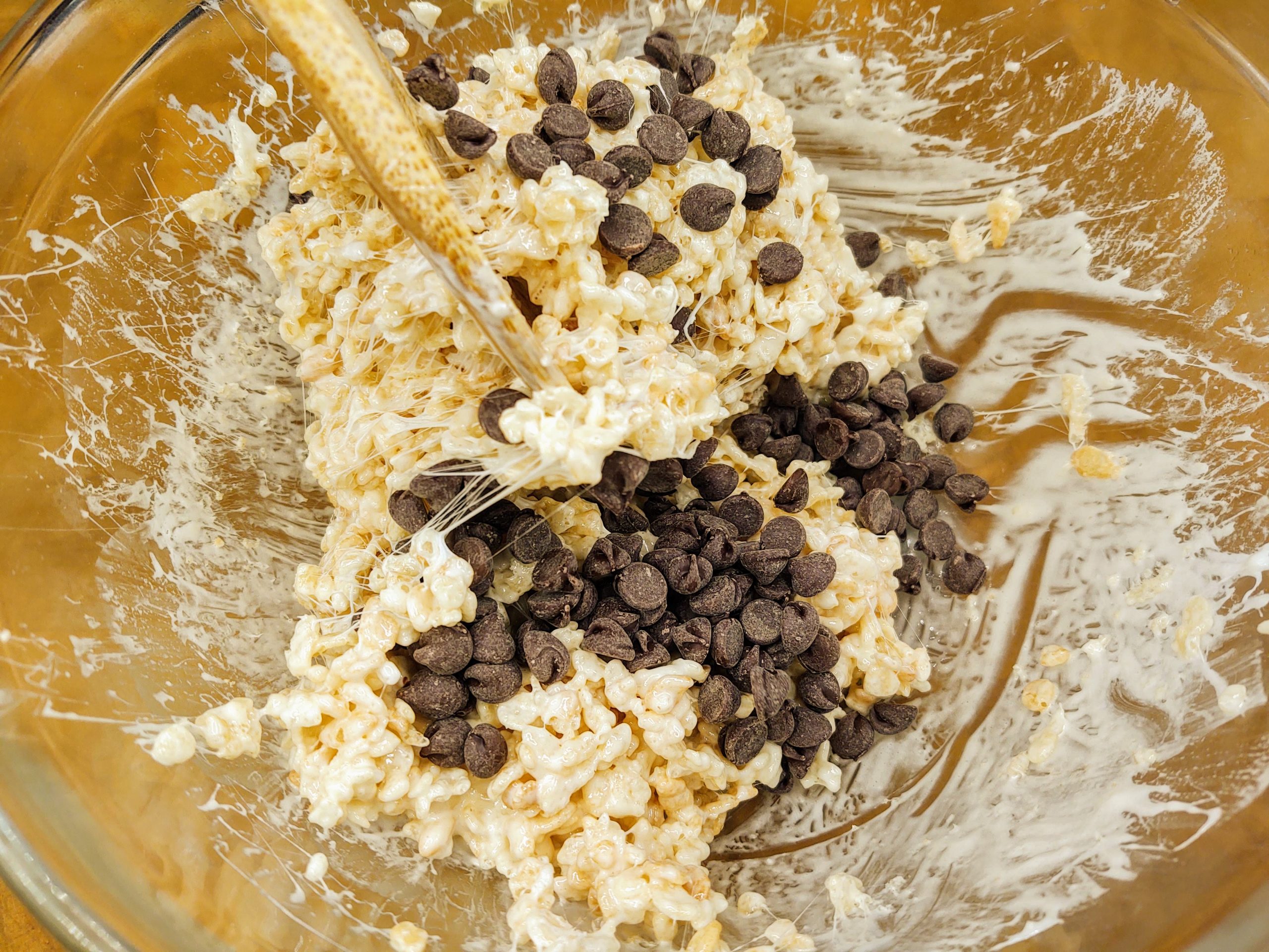 folding chocolate chips in with marshmallows and cereal in a glass bowl