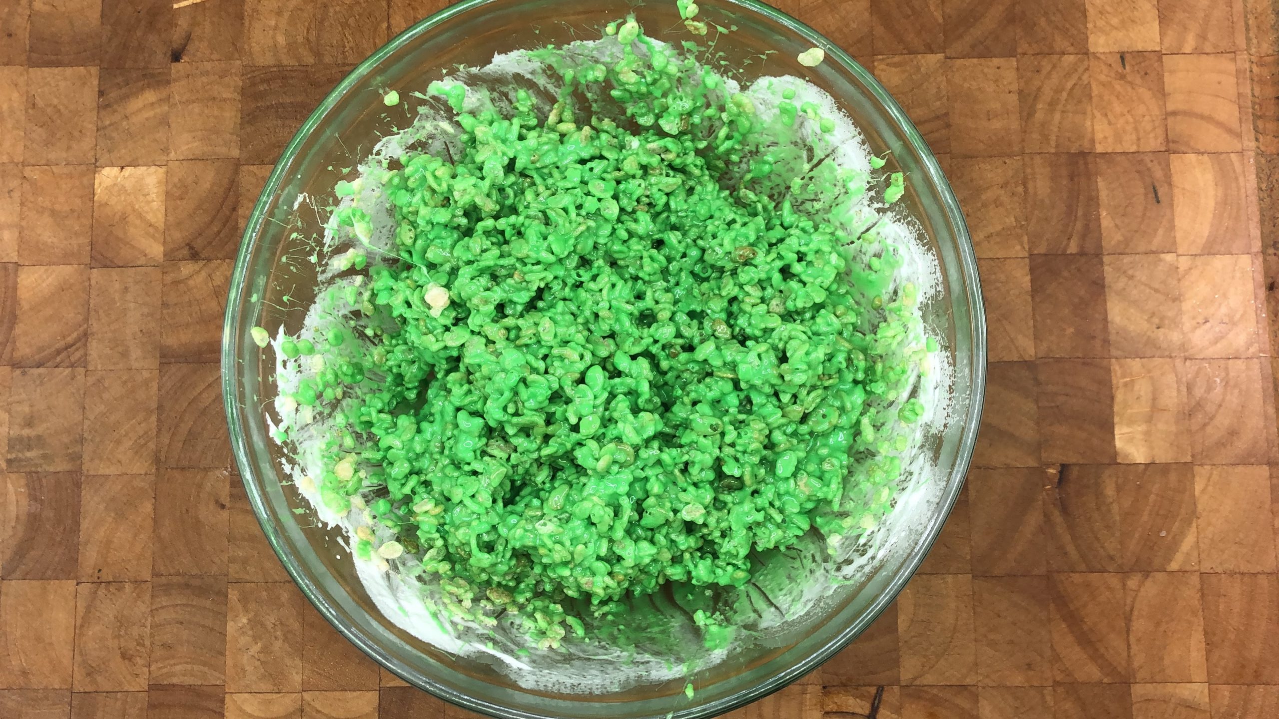 mixing green food coloring, butter, marshmallows and cereal in a bowl