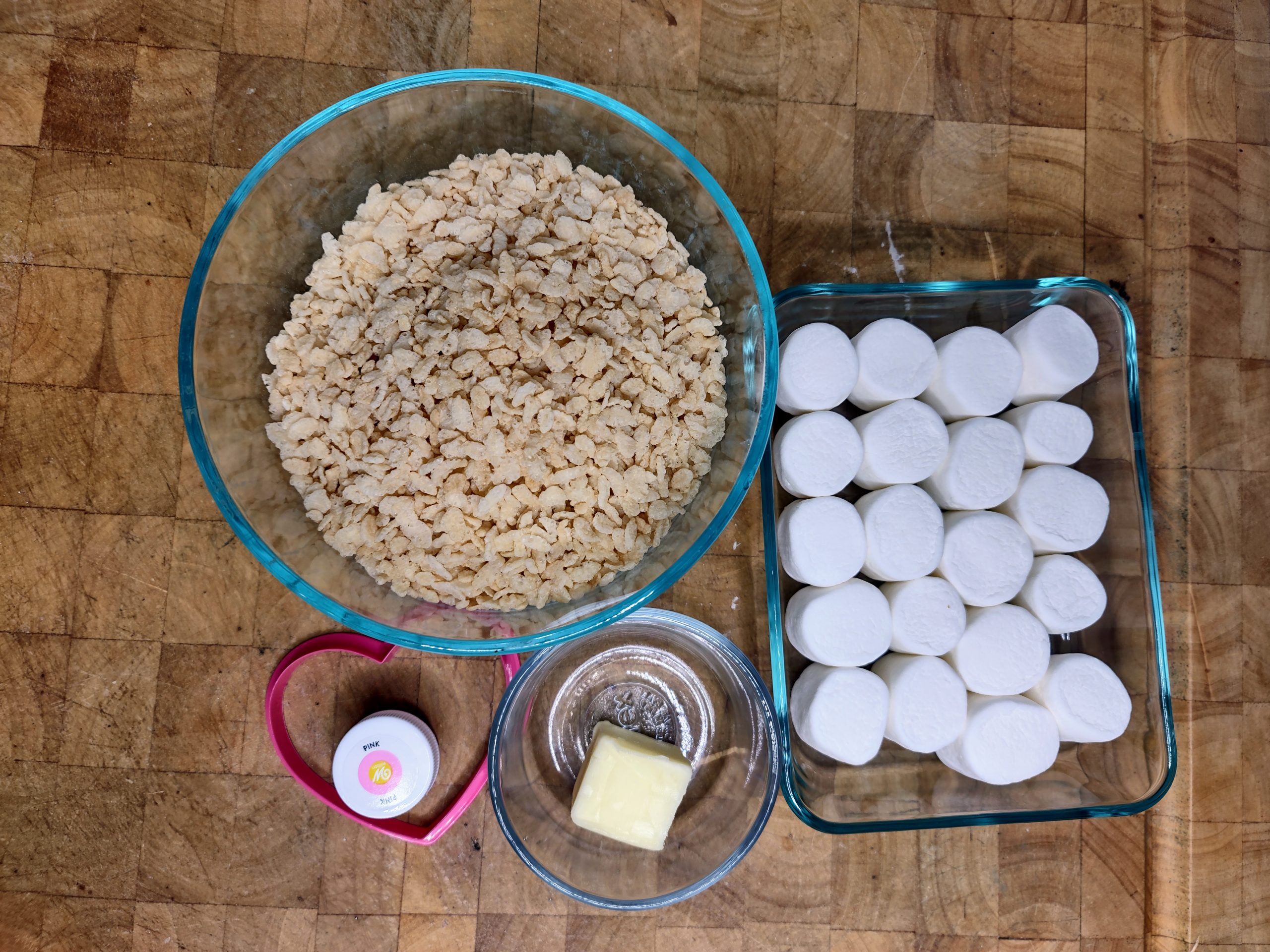 bowls of butter, marshmallows and rice krispie cereal as well as pink food coloring and heart cookie cutter