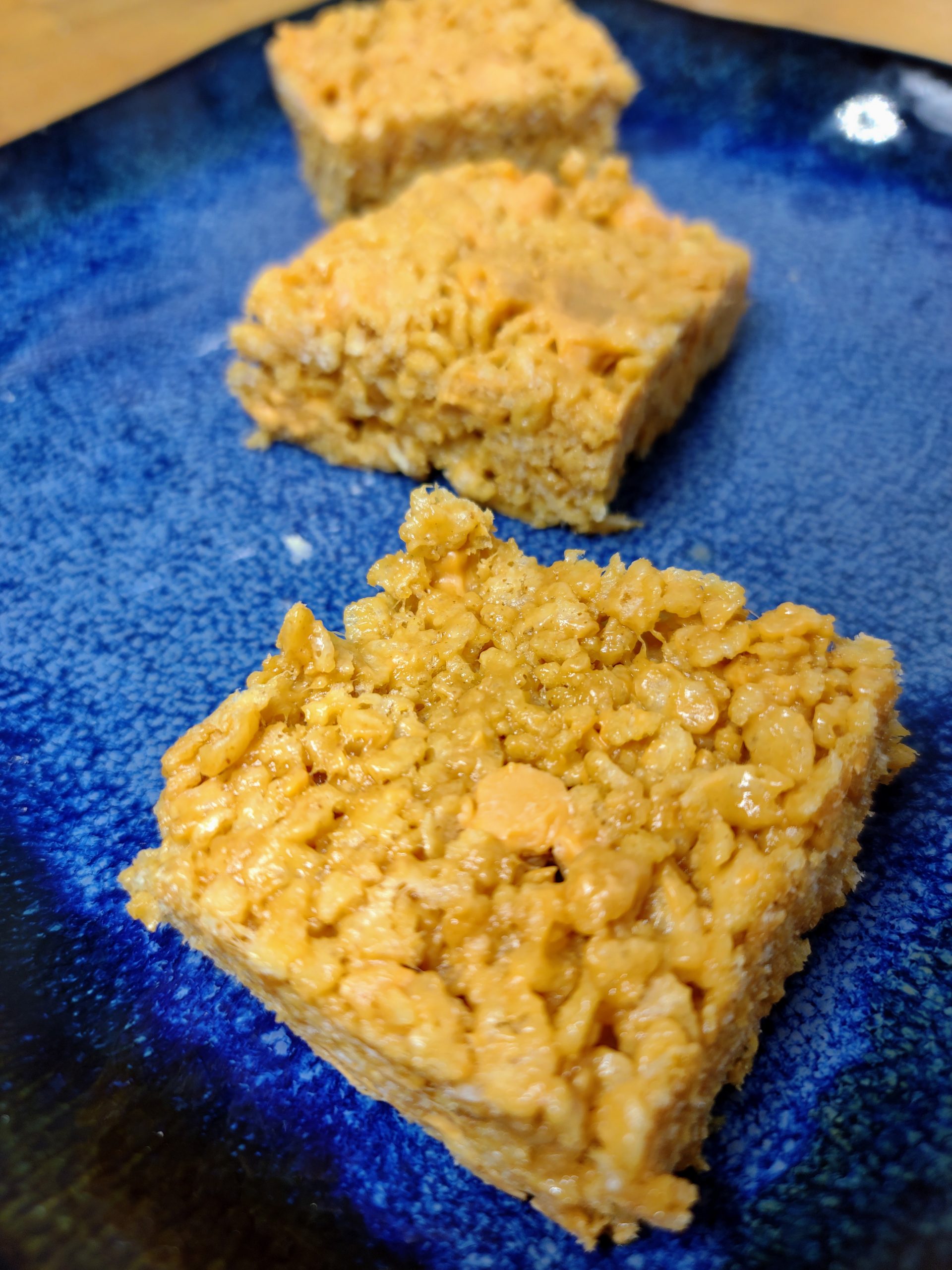 three peanut butter butterscotch rice krispie treats on a blue plate