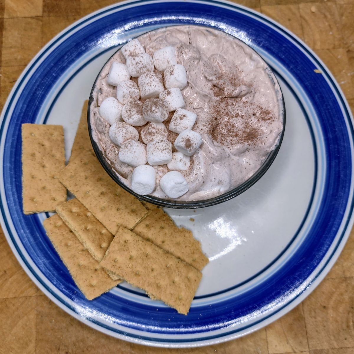 Hot chocolate dip in a bowl on a plate next to graham crackers.