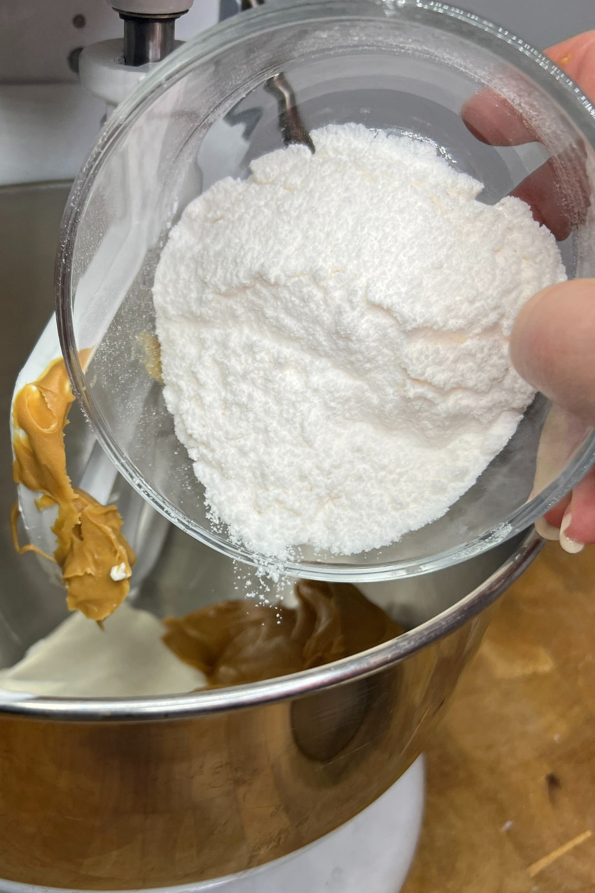 Pouring powdered sugar into a mixing bowl with peanut butter.