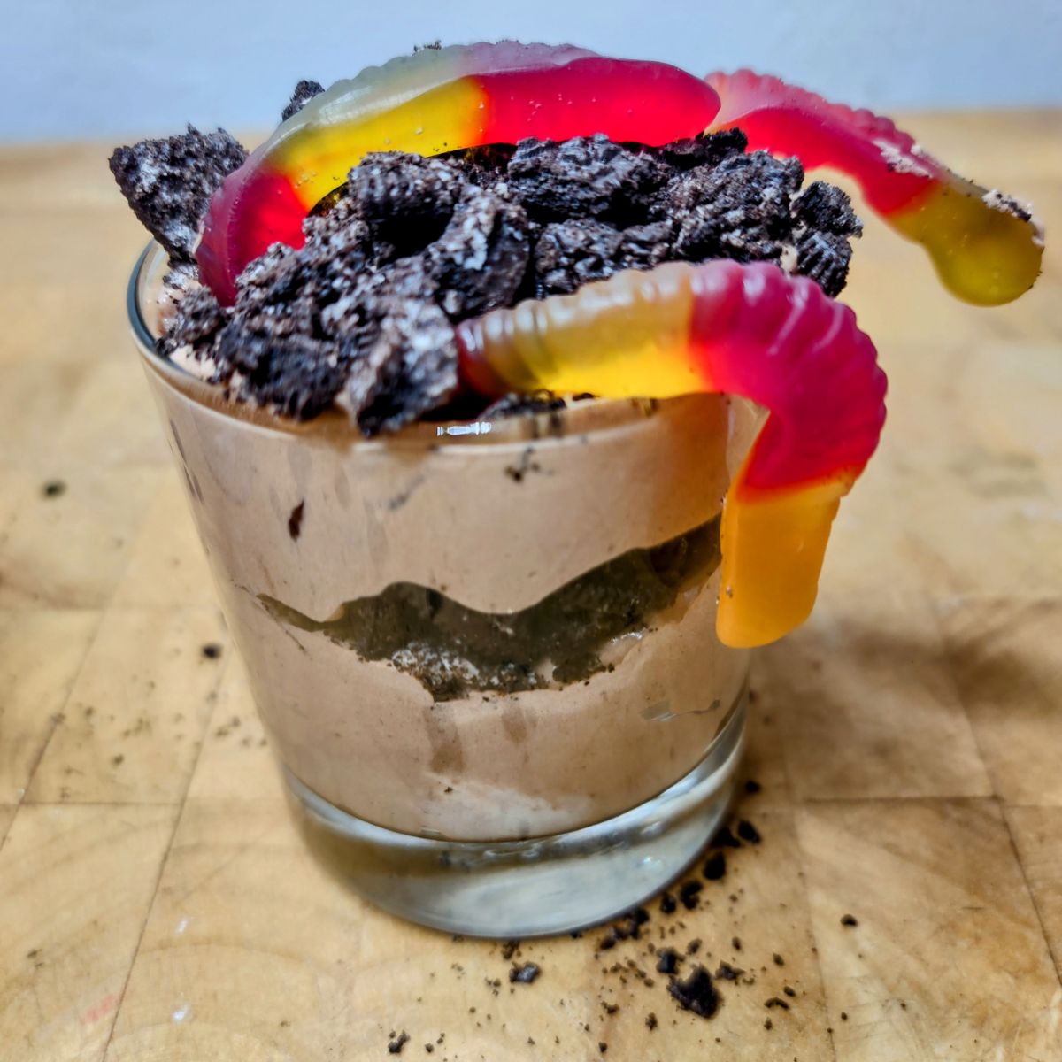 Pudding dirty cup with gummy worms on a wooden table.