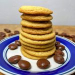 Milk dud cookies stacked on a plate surrounded by milk duds.