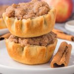 Two mini apple pie tarts stacked on a plate with a cinnamon stick.