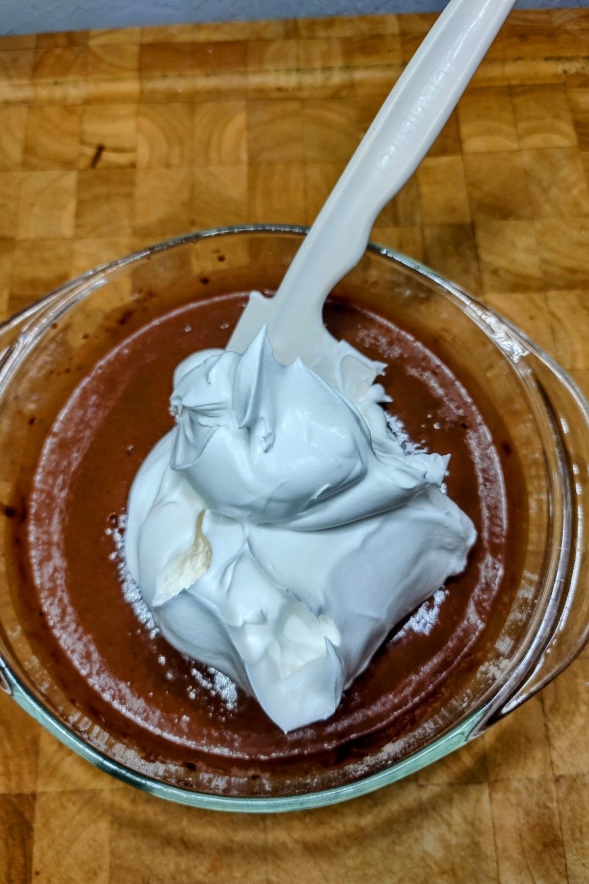 Adding whipped topping to chocolate pudding in a mixing bowl.