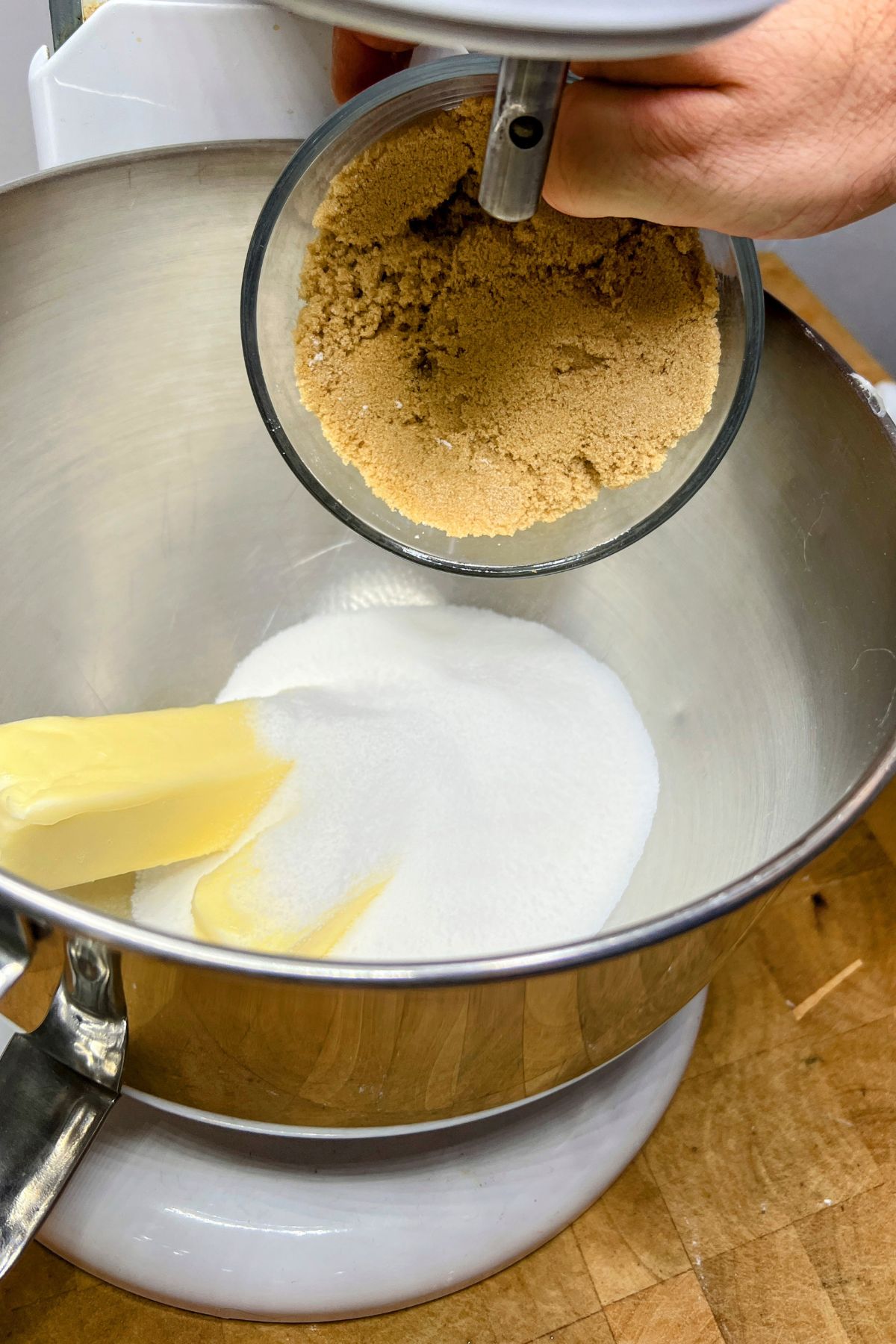 Adding brown sugar to mixing bowl with white sugar and butter.