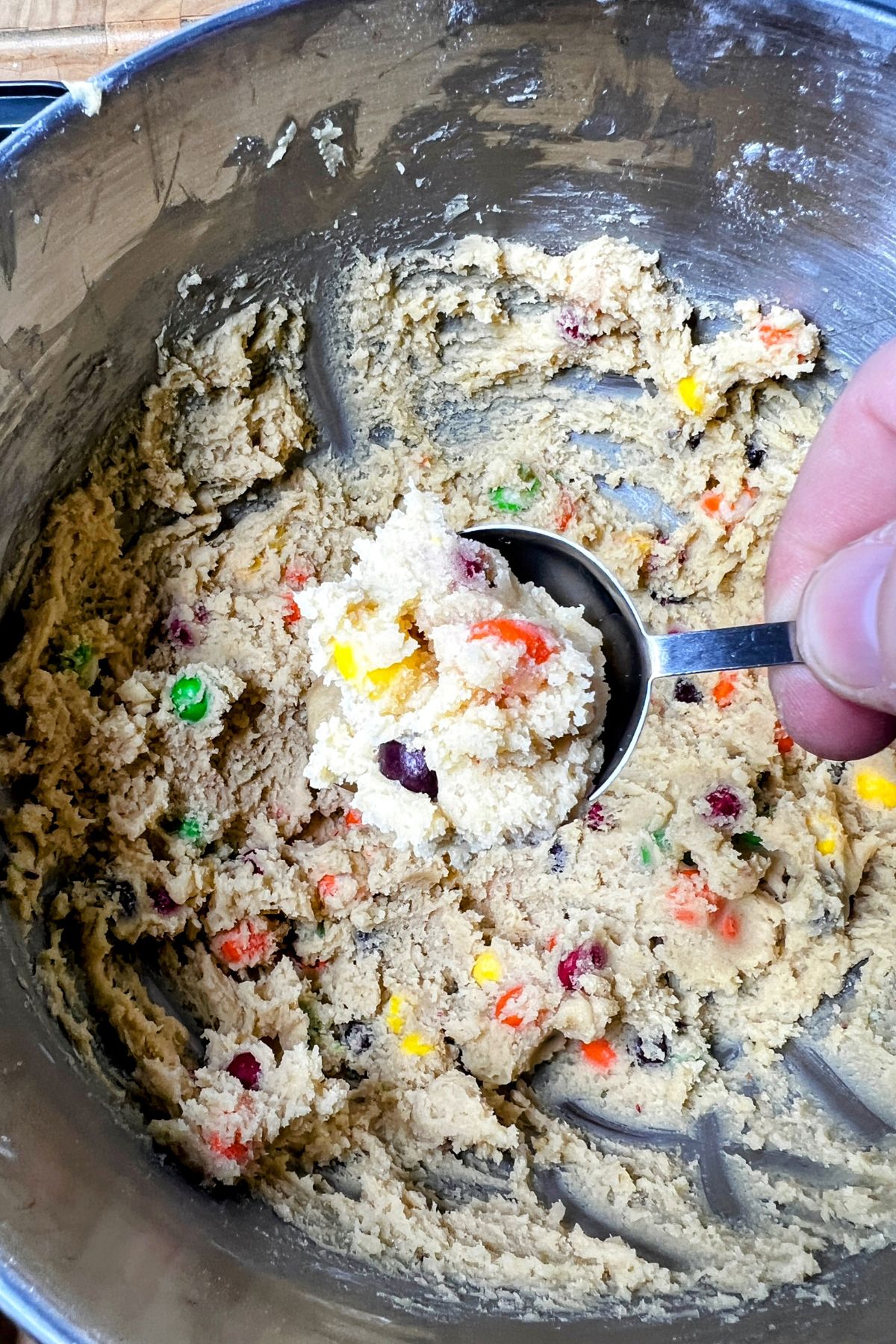 Scooping skittle cookie dough with a tablespoon.