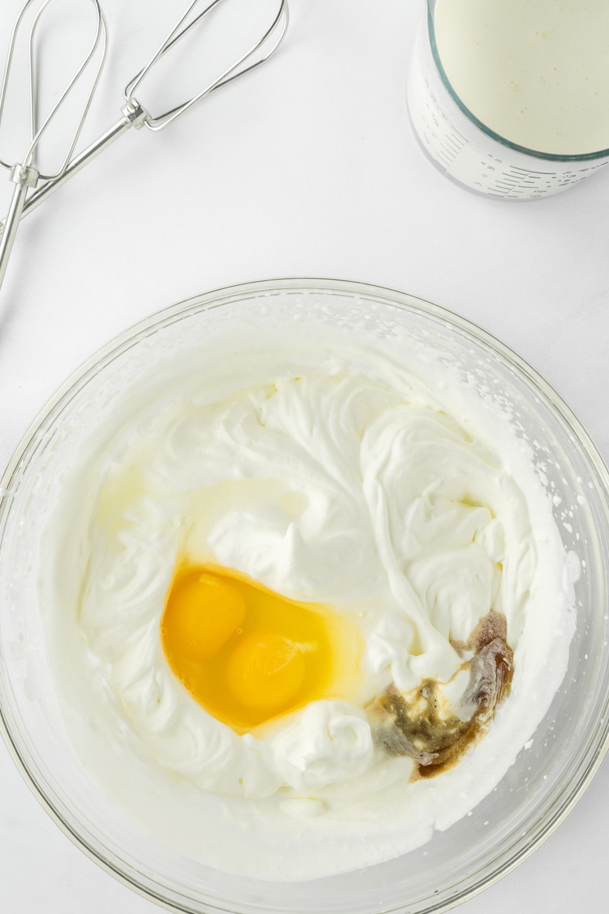 Eggs and vanilla in bowl with creamed sugar and butter.