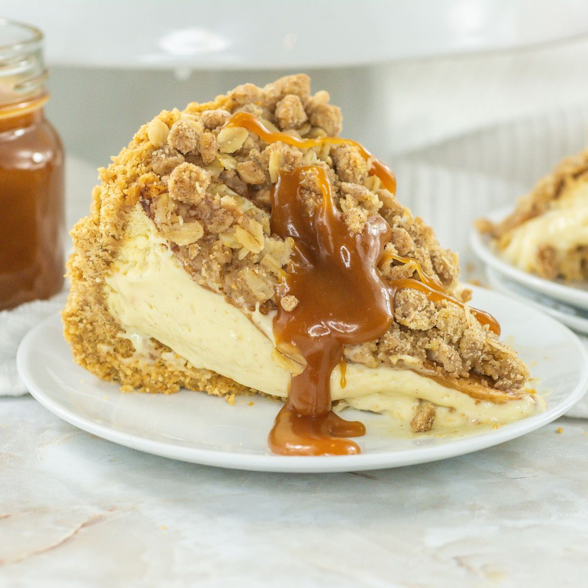 Slice of apple crunch cheesecake with caramel sauce on top.