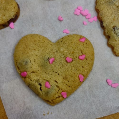 Heart shaped chocolate chip cookie with sprinkles on parchment paper.