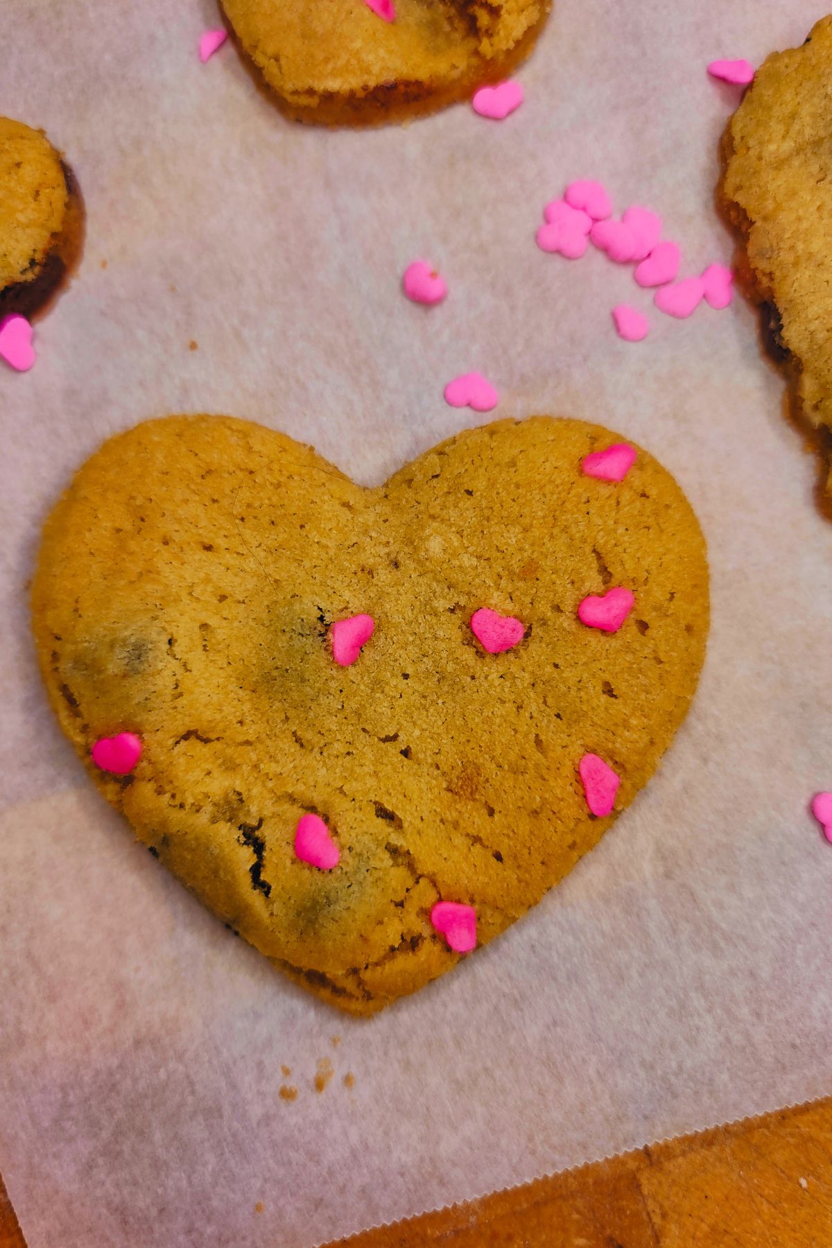 Heart shaped chocolate chip cookie with pink sprinkles on parchment paper.