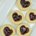 5 heart thumbprint cookies on a white plate.