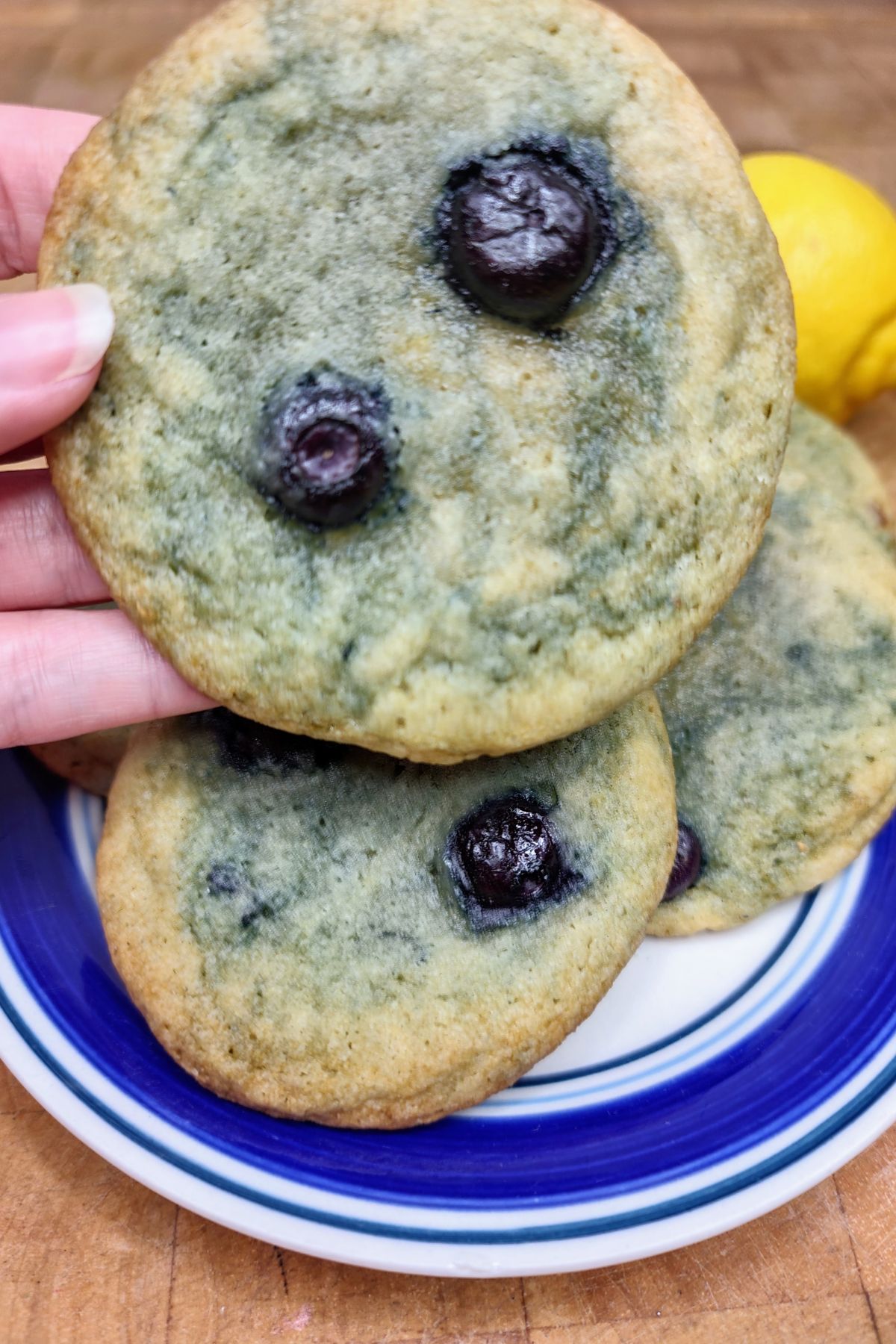 Hand holding a lemon blueberry cookie over a plate.