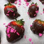 Nutella covered strawberries with sprinkles on parchment paper.