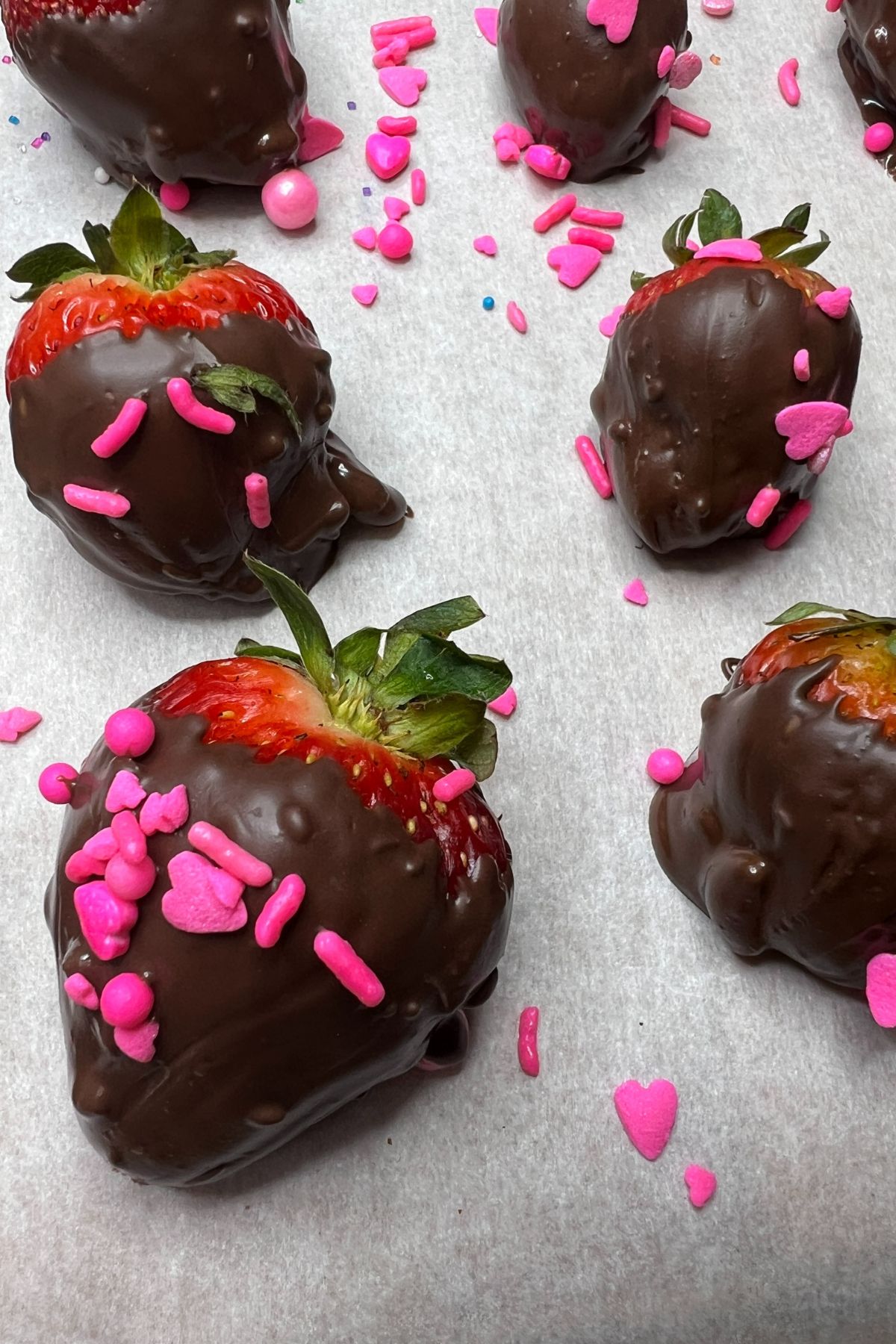 Nutella and chocolate covered strawberries with sprinkles on parchment paper.