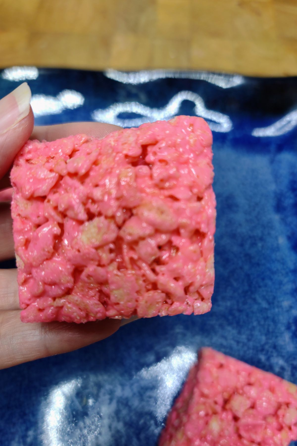 Hand holding a pink rice krispie treat over a blue plate.