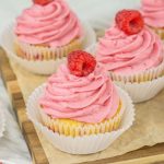 Raspberry cupcakes with raspberry frosting on a cutting board.