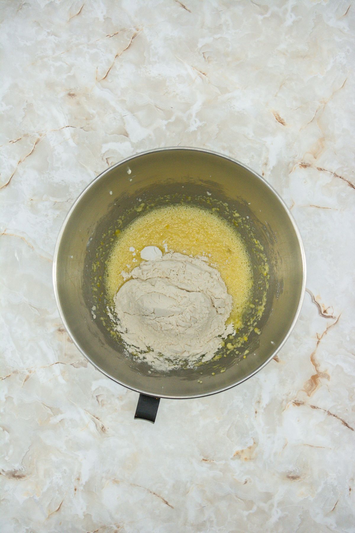 Flour and eggs with creamed sugar and butter in a mixing bowl.