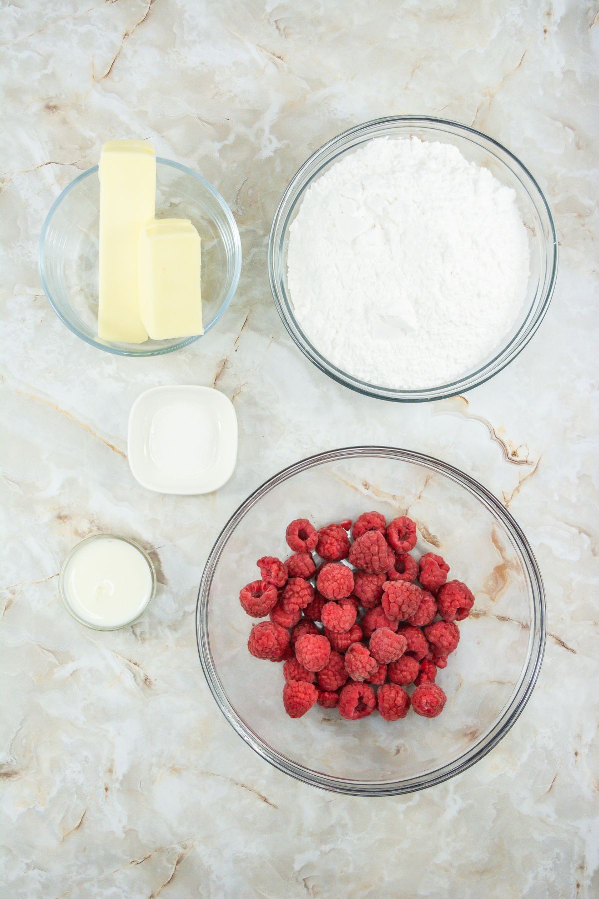 Ingredients for raspberry frosting on a marble table.