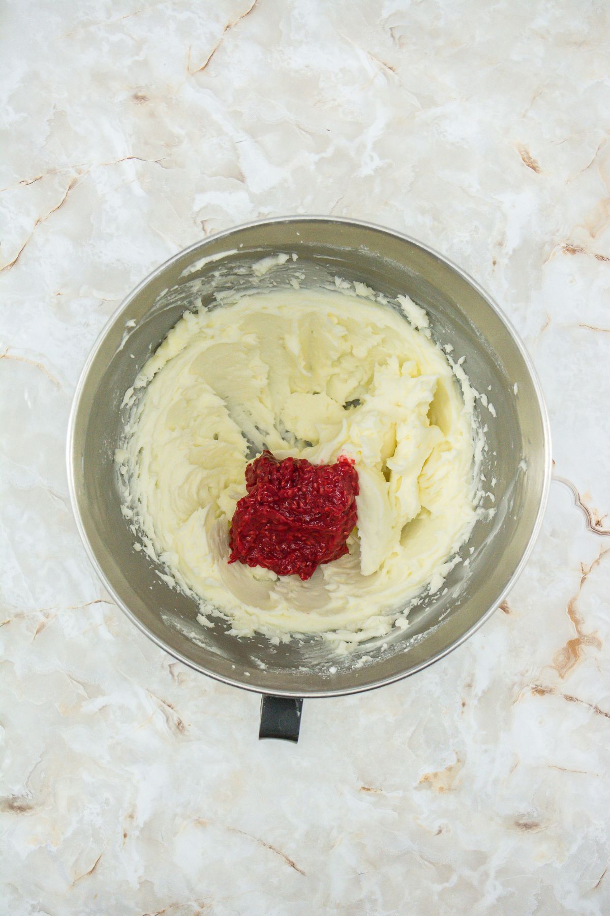 Butter and sugar with raspberry puree in a mixing bowl.