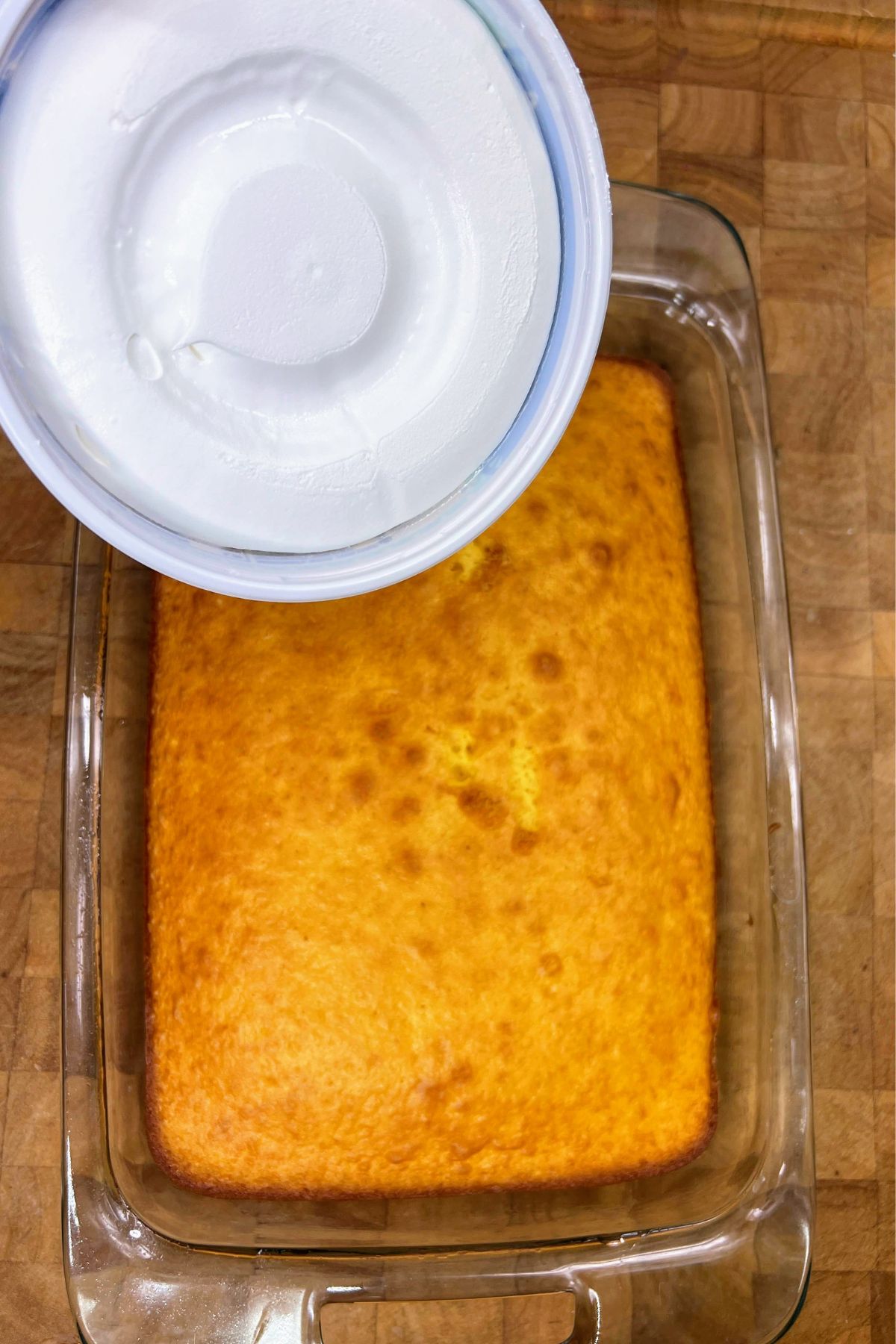 Putting cool whip on baked yellow cake.
