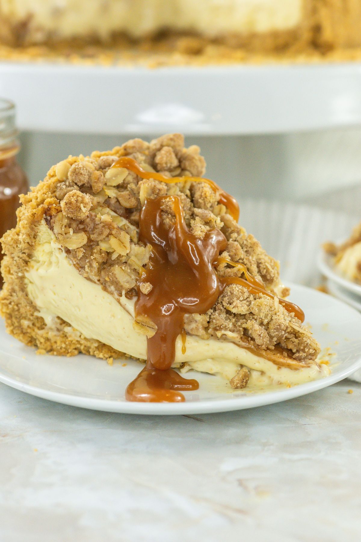 Slice of apple crunch cheesecake on a plate with caramel sauce.