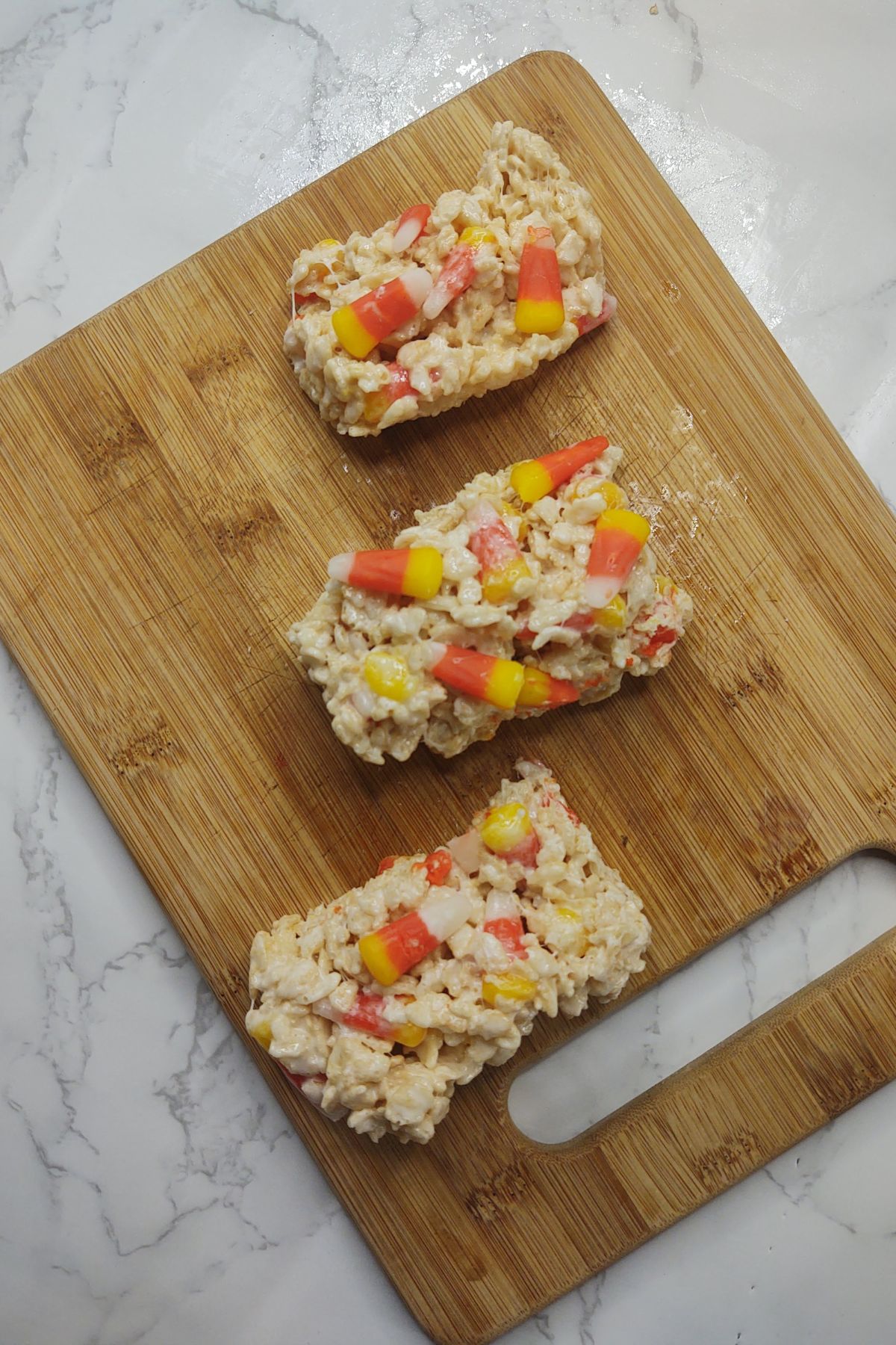 Candy corn rice krispie treats on a wooden cutting board.