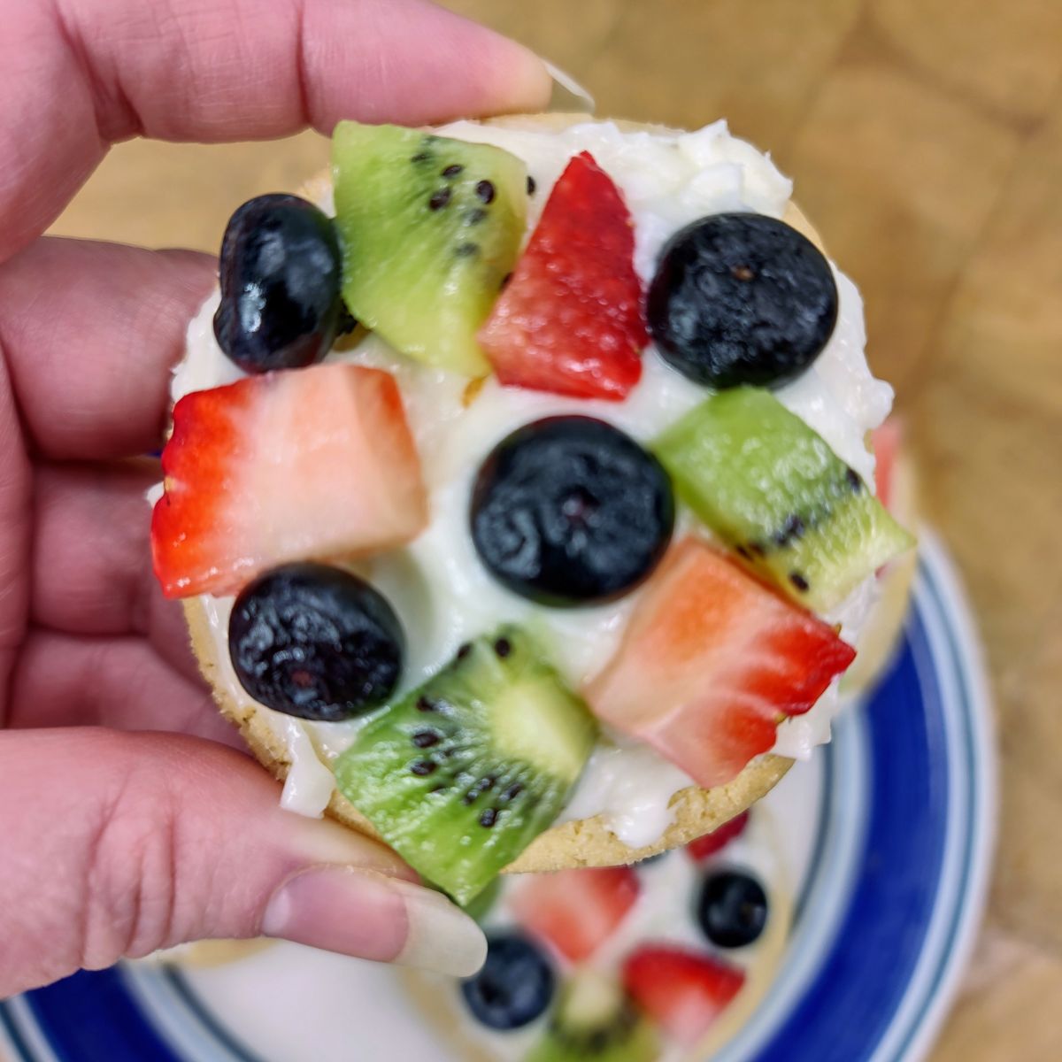 Fruit pizza sugar cookie being held in a hand.