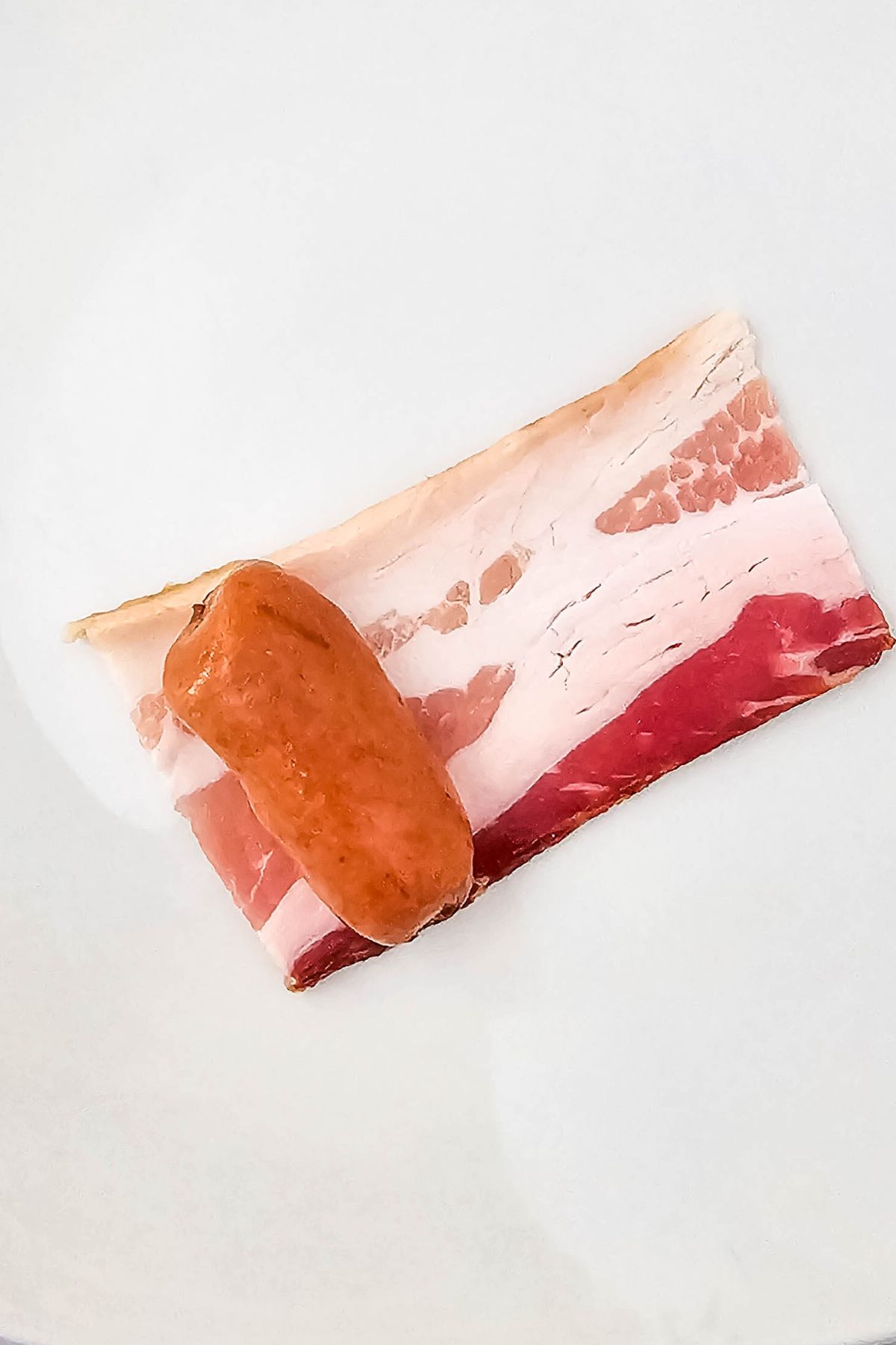 Lil Smokie on top of slice of bacon.