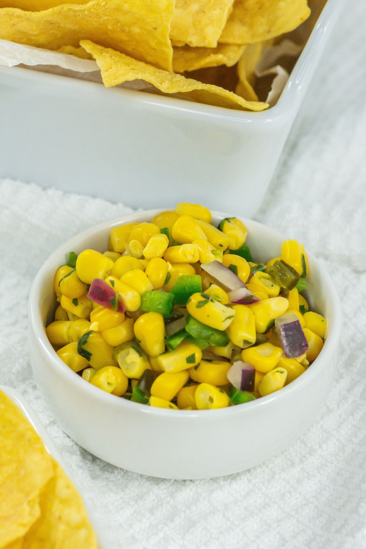 Corn salsa in a white bowl next to chips.