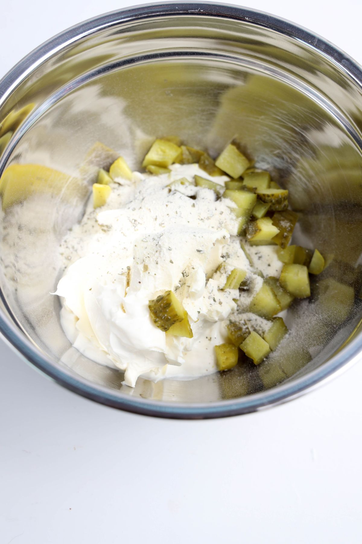Chopped pickles and cream in a mixing bowl.