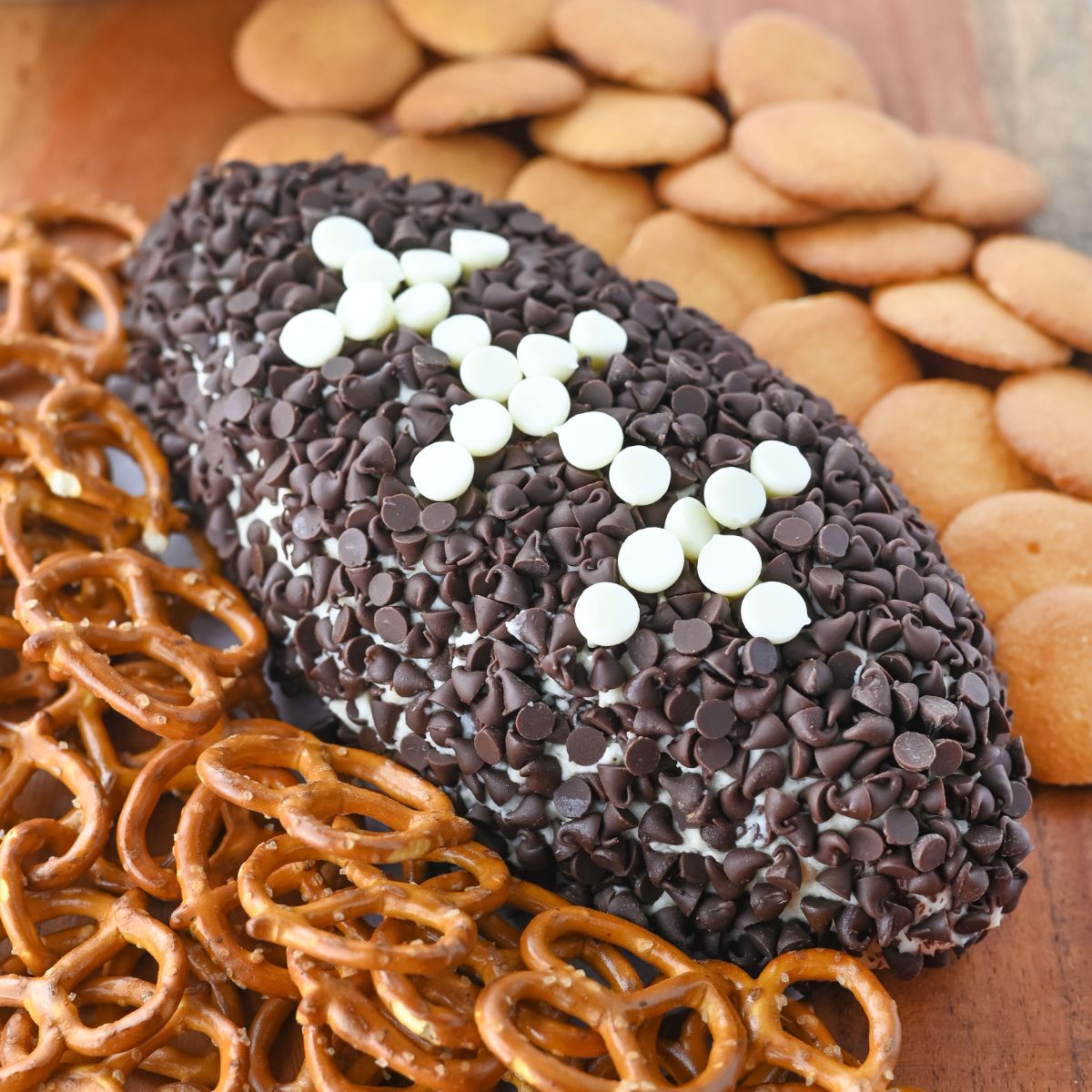 Football cheeseball with pretzels on a wood table.
