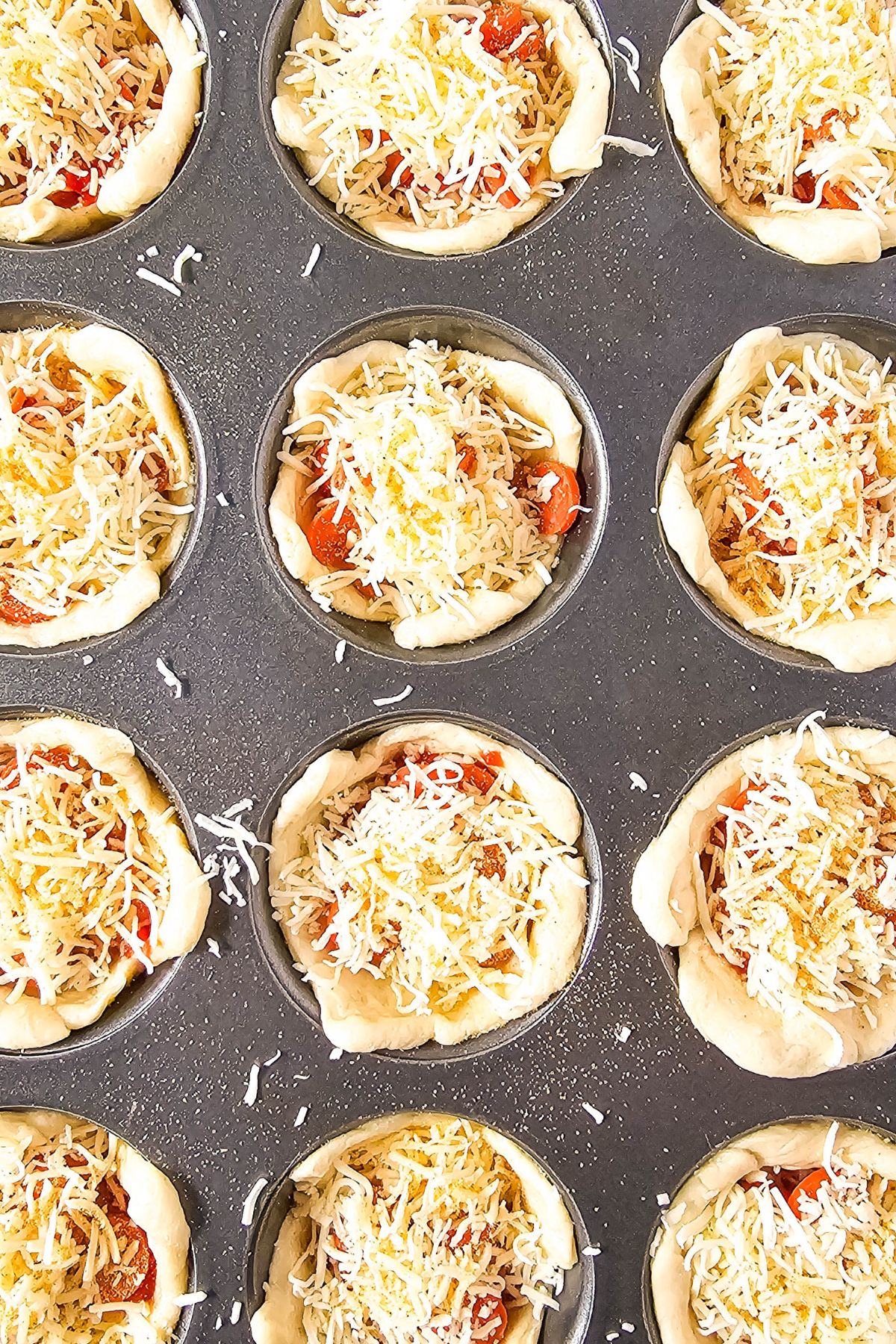 Cheese sprinkled over pepperoni pizza puffs.