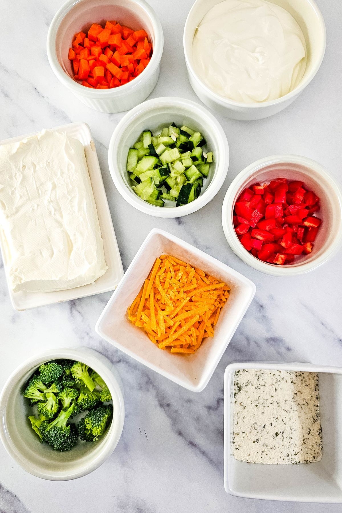 Veggie pizza dip ingredients on a marble counter.