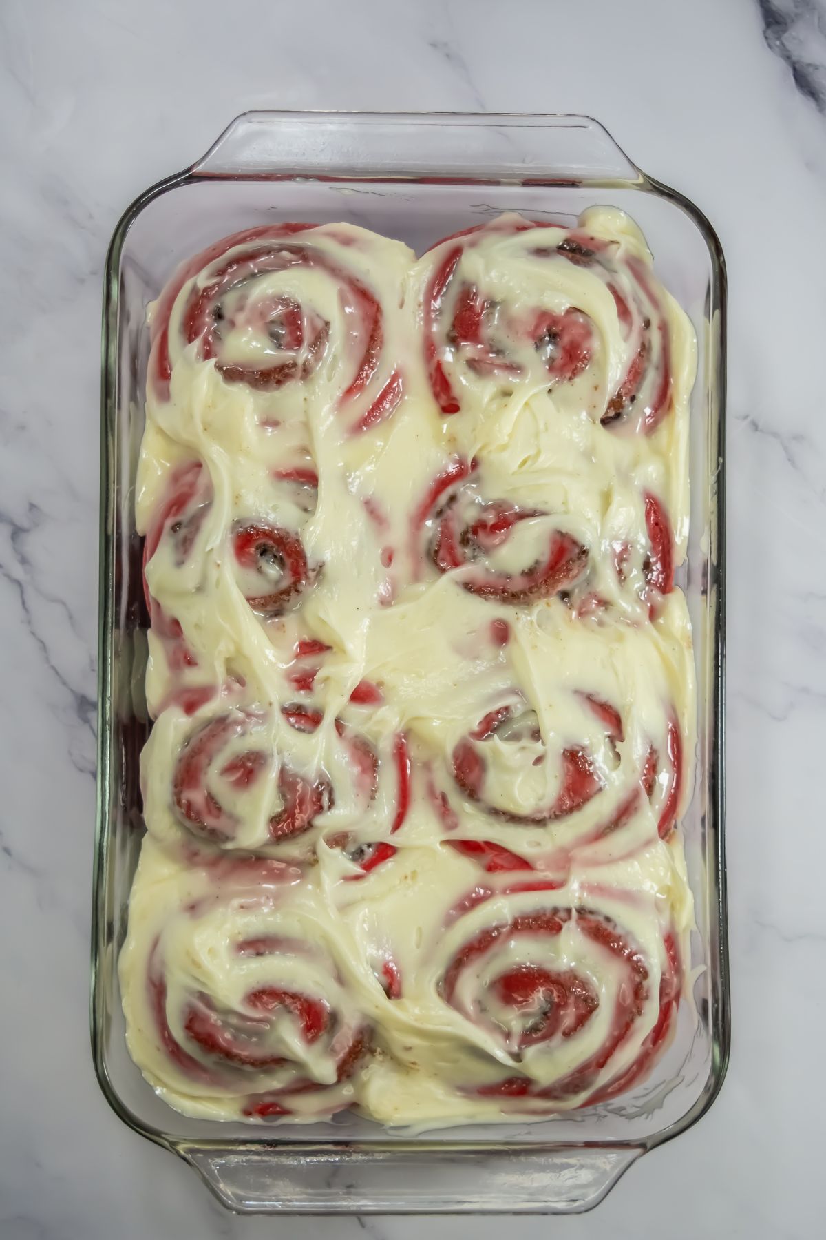 Frosting spread on red velvet cinnamon rolls.