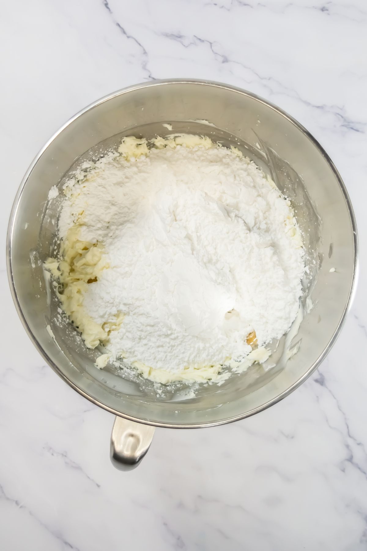 Sugar added to frosting in a bowl.