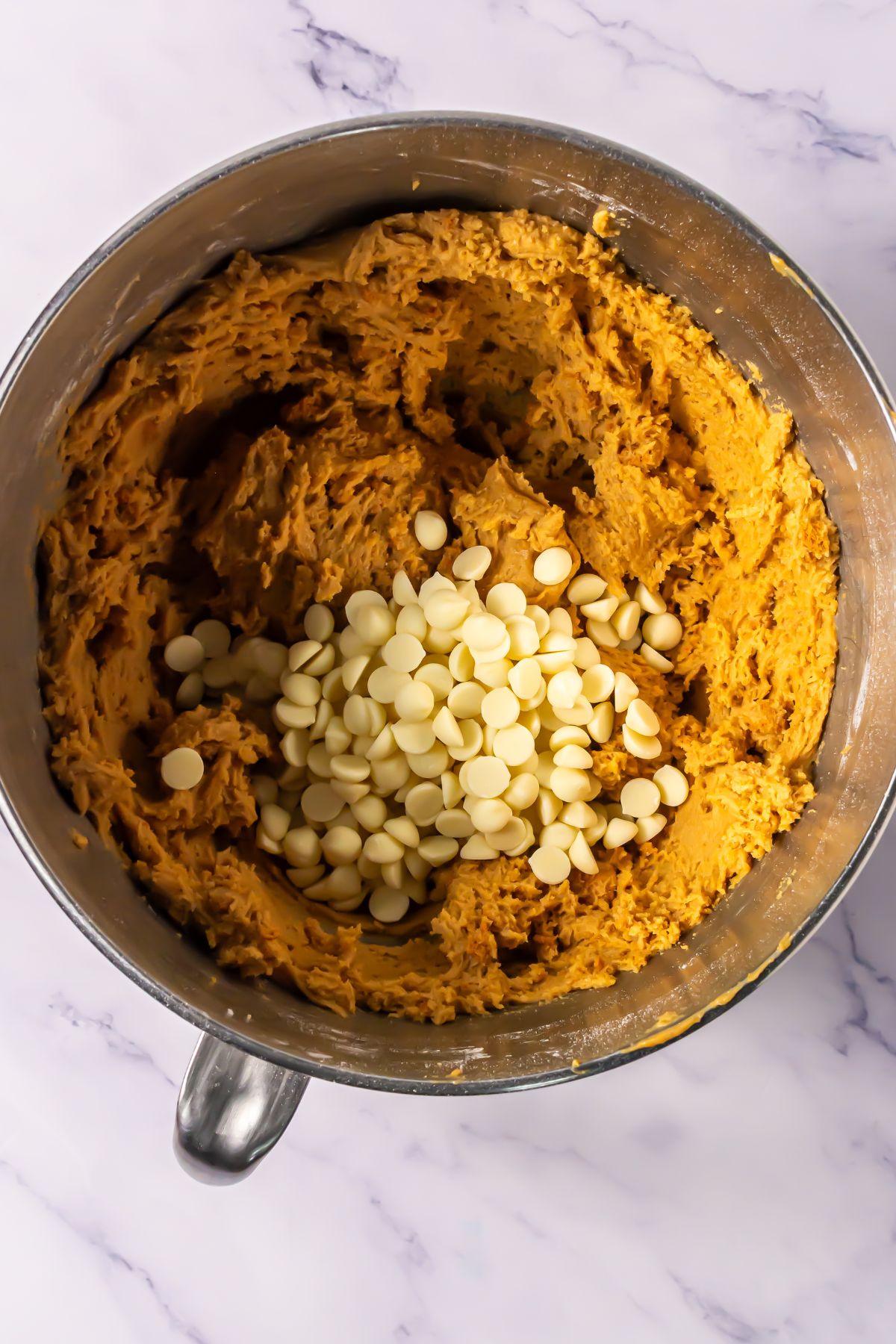 Adding white chocolate chips to cookie dough in a bowl.