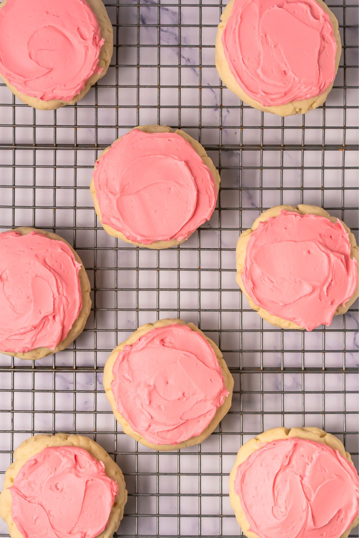 Crumbl sugar cookies with pink icing on a cooling rack.