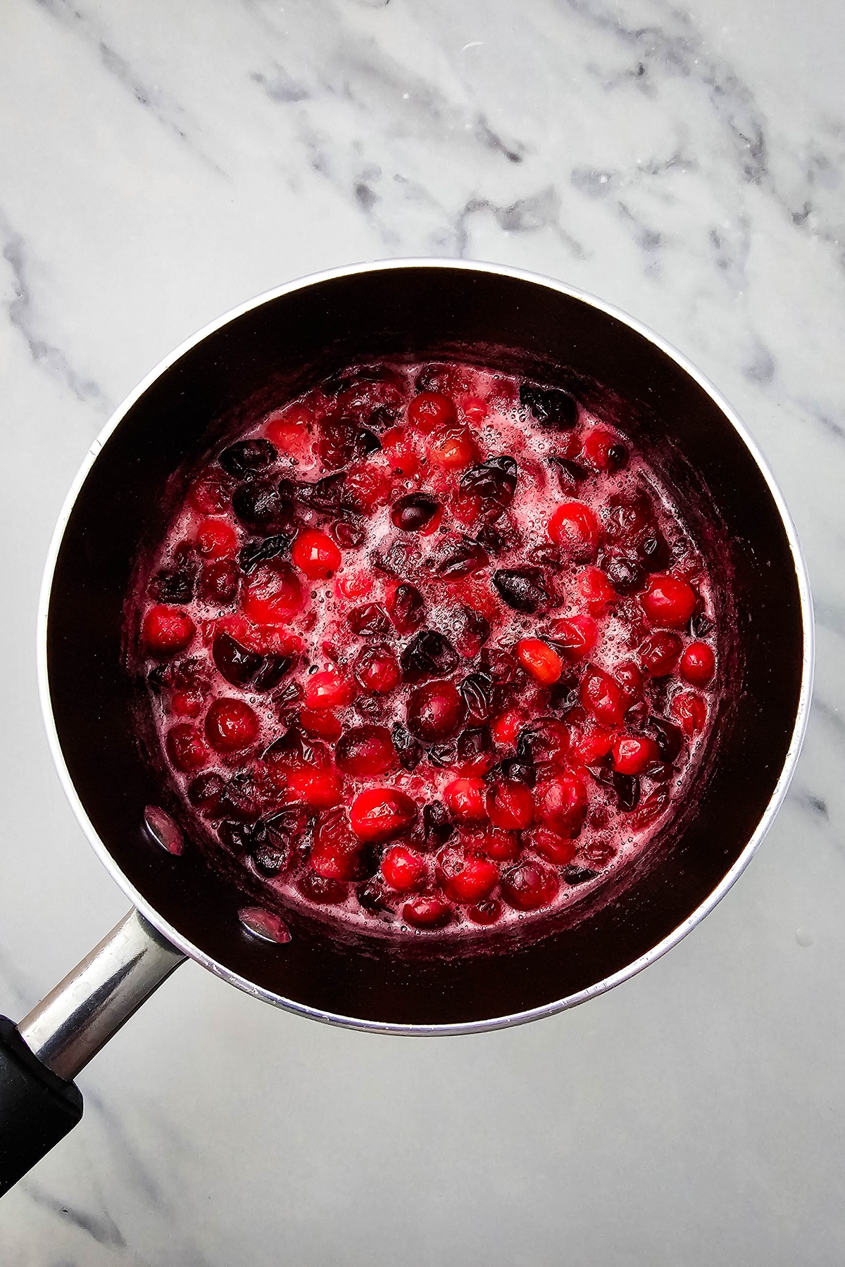 Cranberries and dried fruit simmering in liquid in a saucepan, with some berries beginning to burst.
