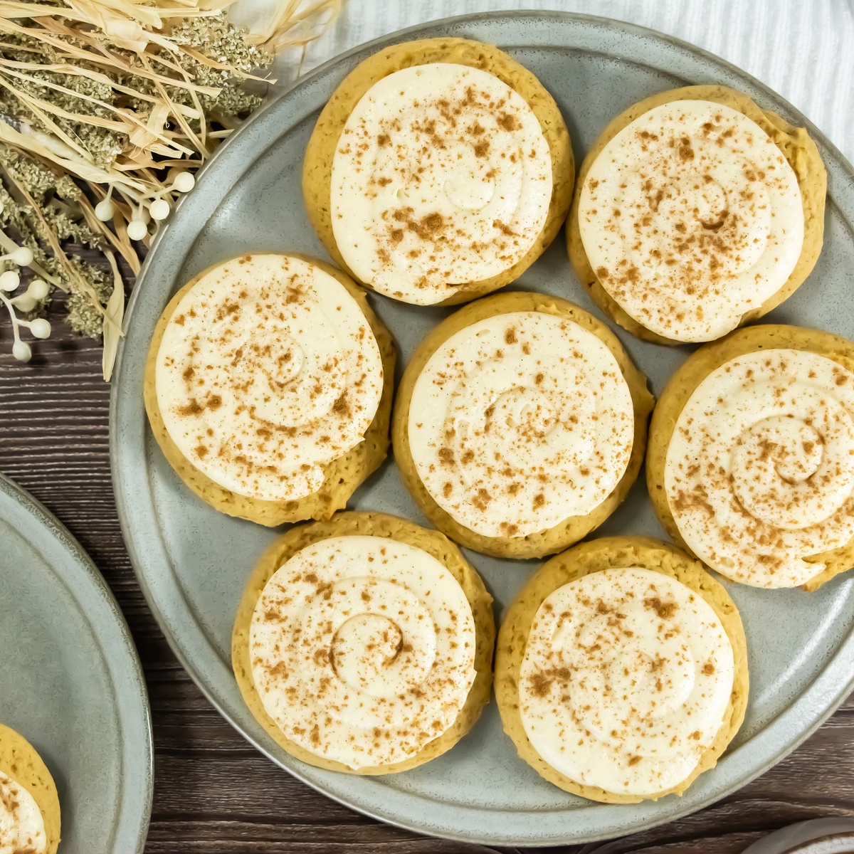 Frosted pumpkin cookies topped with cream cheese icing and dusted with spices, arranged on a gray plate.