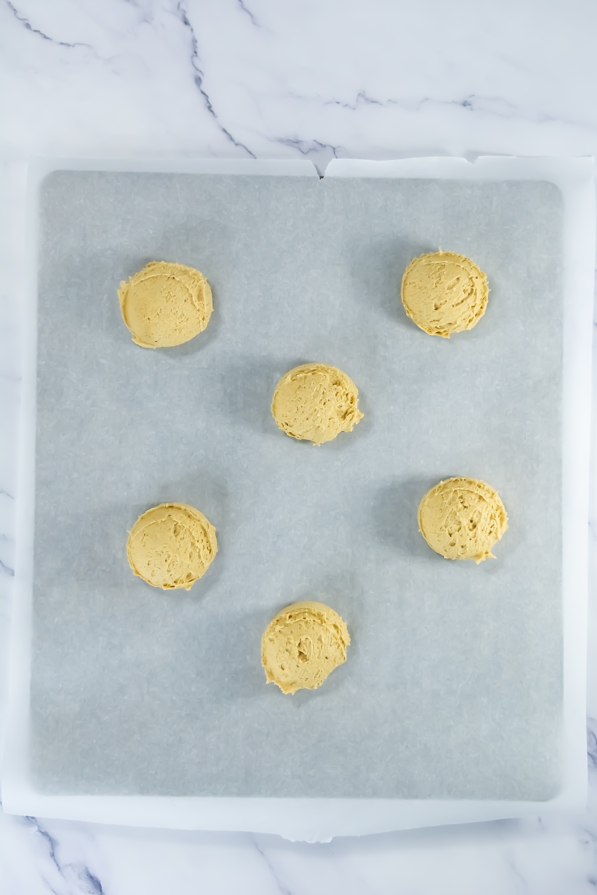 Six scoops of raw pumpkin cookie dough spaced apart on a parchment-lined baking sheet, ready to bake.