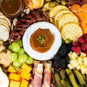 Fall Charcuterie board with brie topped with pumpkin butter, crackers, cured meats, grapes, berries, cheese cubes, and pickles.