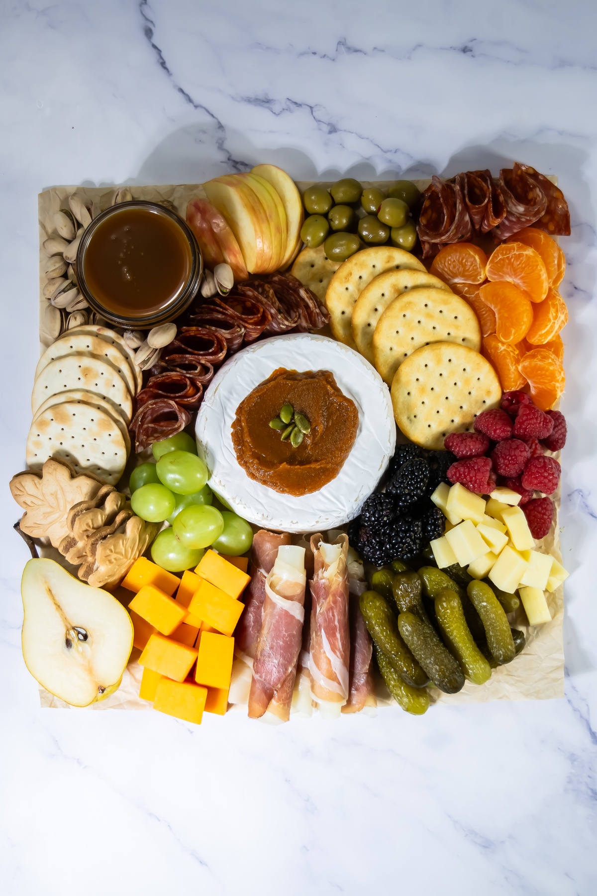 Fall charcuterie board with brie topped with pumpkin butter, cured meats, cheddar cubes, crackers, grapes, pear and more.