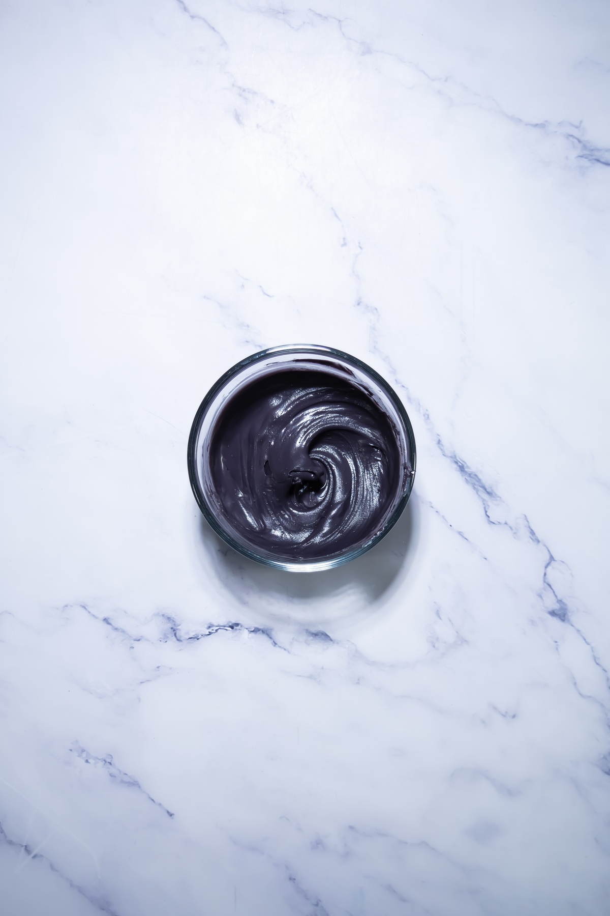 Dark purple or black melted coating in a small glass bowl on white marble surface, swirled and ready for dipping.