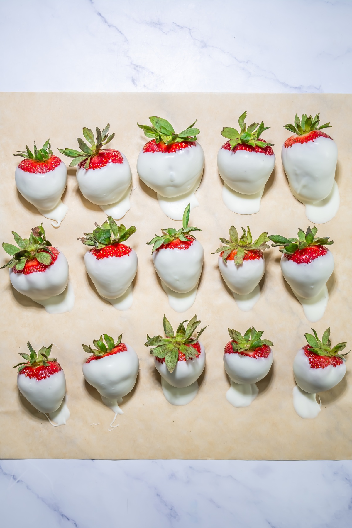 Fifteen strawberries dipped in white chocolate arranged in rows on parchment paper.